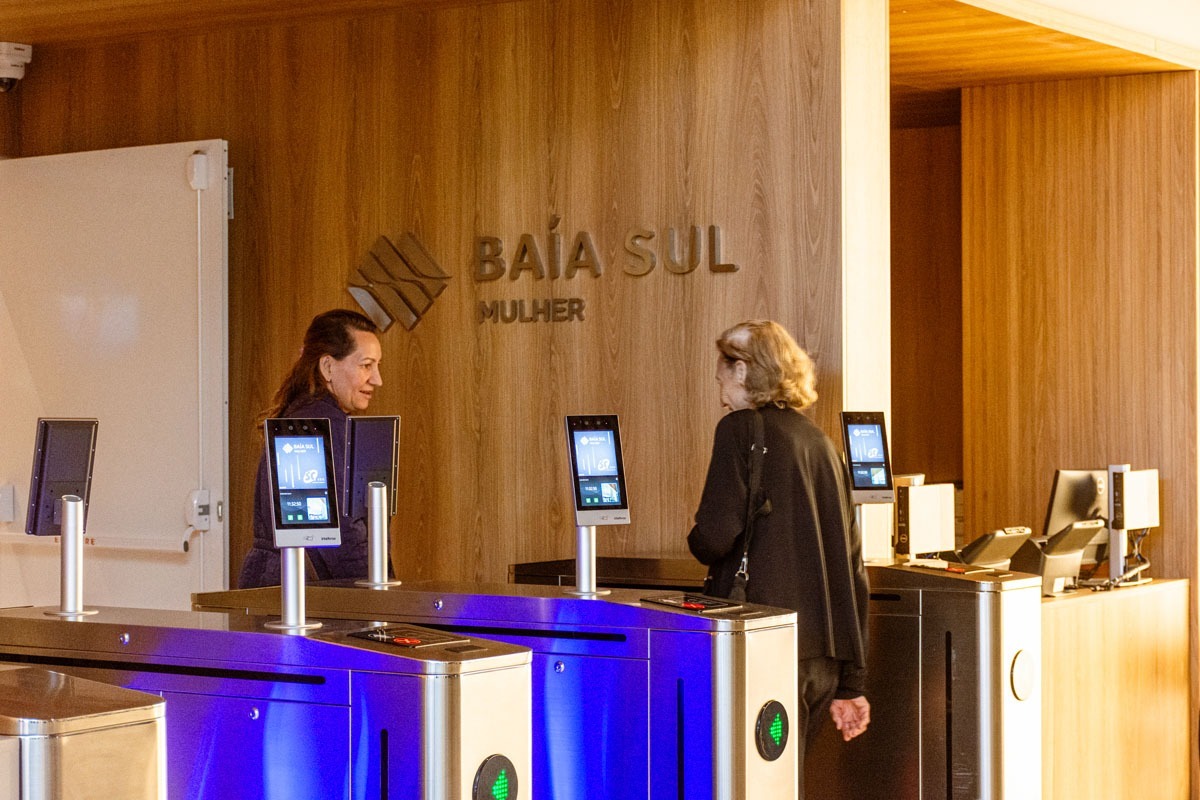 Fotografia de recepção do Baía Sul Mulher, com catracas de acesso e duas mulheres conversando.