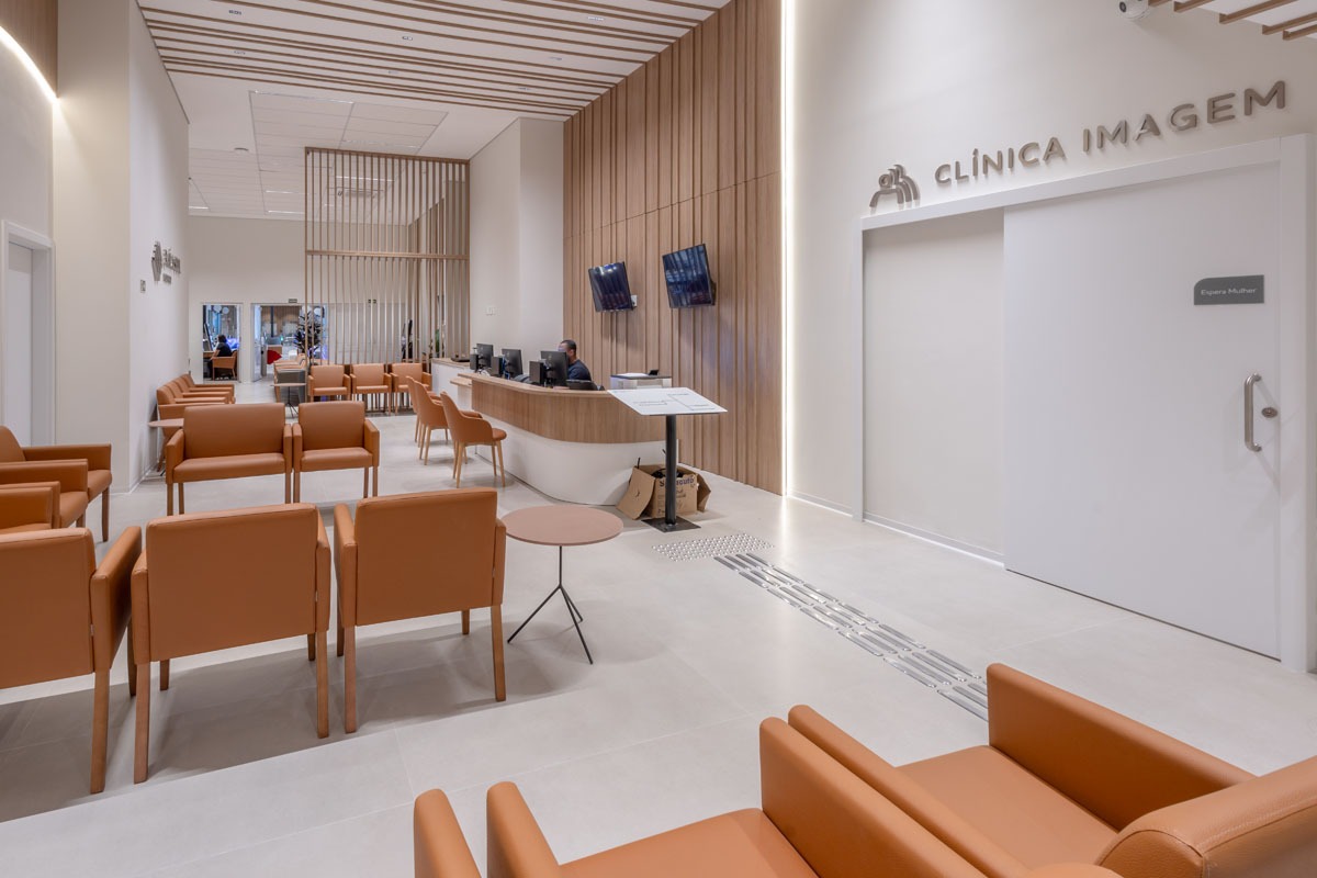 Fotografia de sala de espera da Clínica Imagem, com recepção, poltronas laranja e painéis de madeira.
