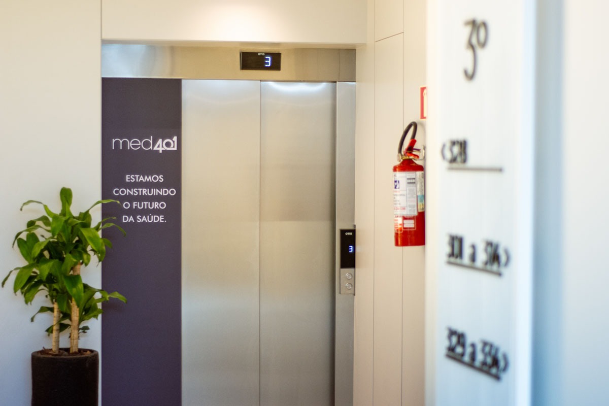 Fotografia de elevador em prédio de saúde, com banner da Medquatro e texto: “Estamos construindo o futuro da saúde.”